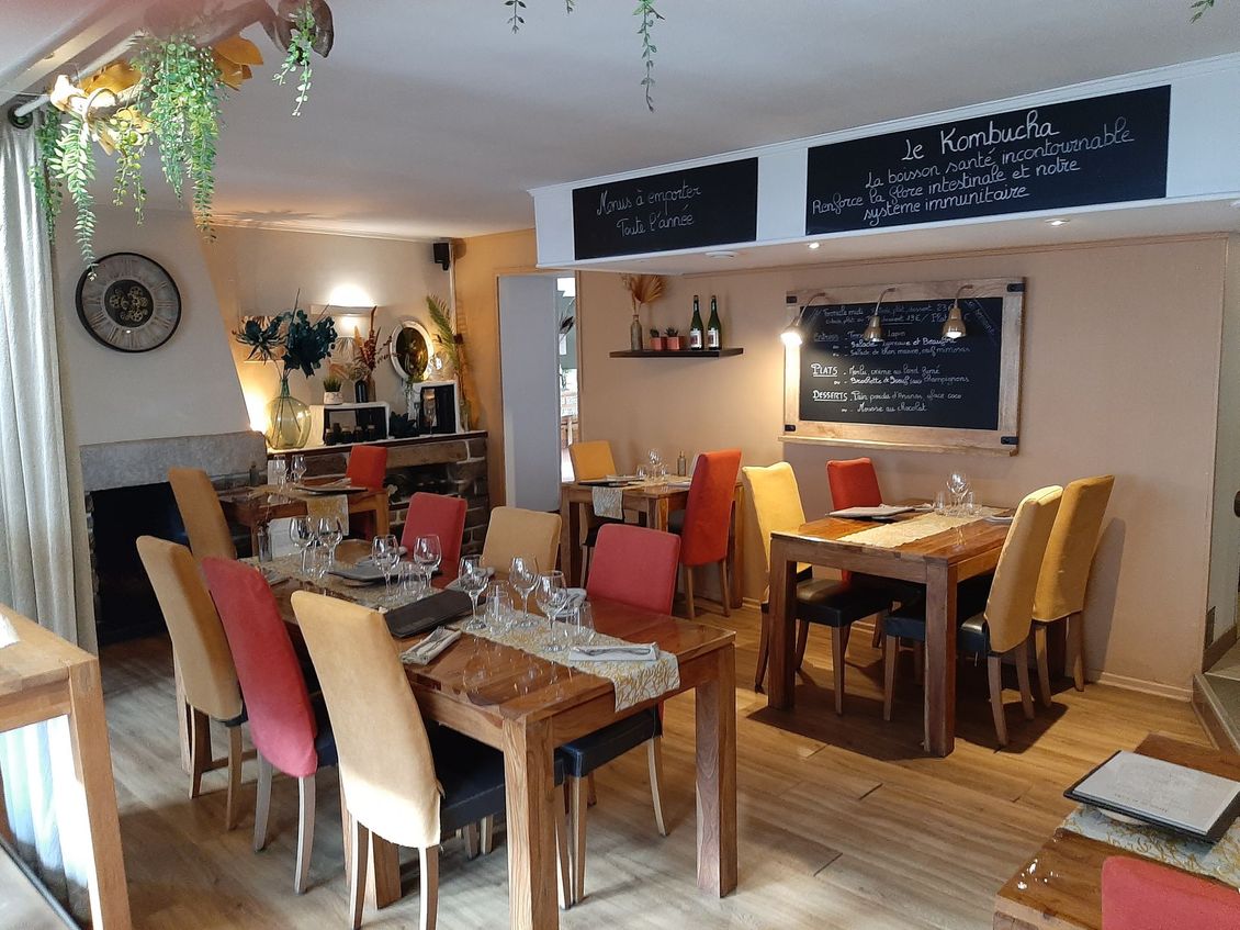 Un intérieur de restaurant chaleureux avec des tables et des chaises en bois, agrémenté de tissus d'ameublement rouges et jaunes et de plantes suspendues.