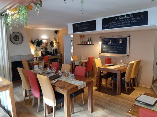 Un intérieur de restaurant chaleureux avec des tables et des chaises en bois, agrémenté de tissus d'ameublement rouges et jaunes et de plantes suspendues.