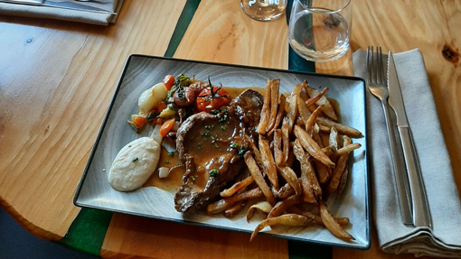 Un repas servi à l'assiette, composé d'un steak nappé de sauce, de frites croustillantes, d'une portion de purée et de tomates cerises rôties.