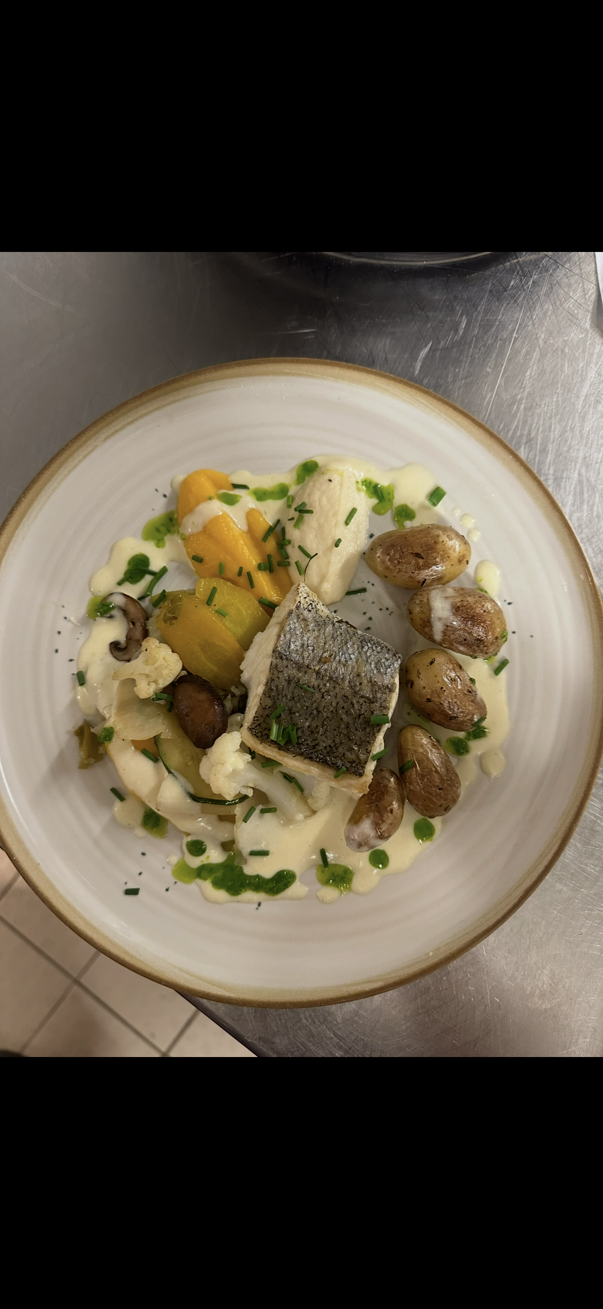 Un plat composé d'un morceau de poisson avec la peau, servi sur une sauce crémeuse avec des pommes de terre rôties et des légumes.