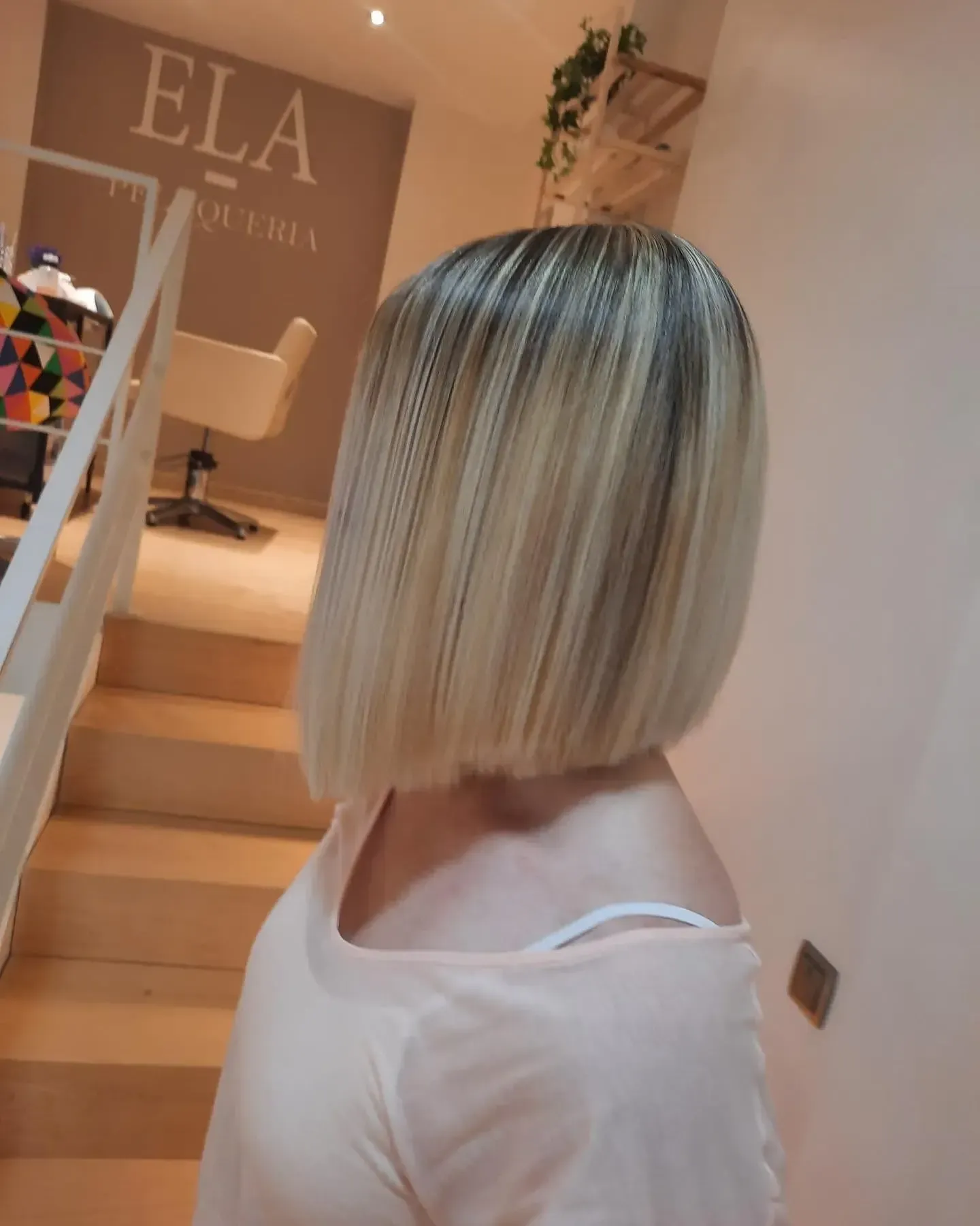 Corte de pelo bob rubio con raíces oscuras en un salón de belleza.