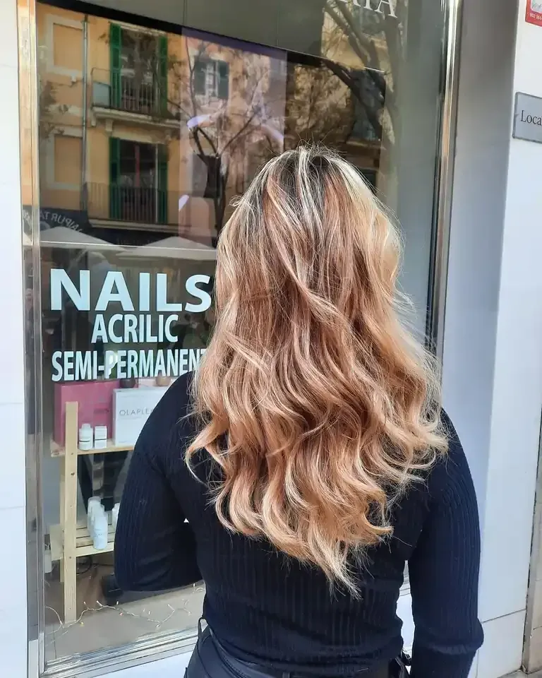 Una mujer con cabello castaño claro y ondulado se encuentra frente a la ventana de un salón de uñas.