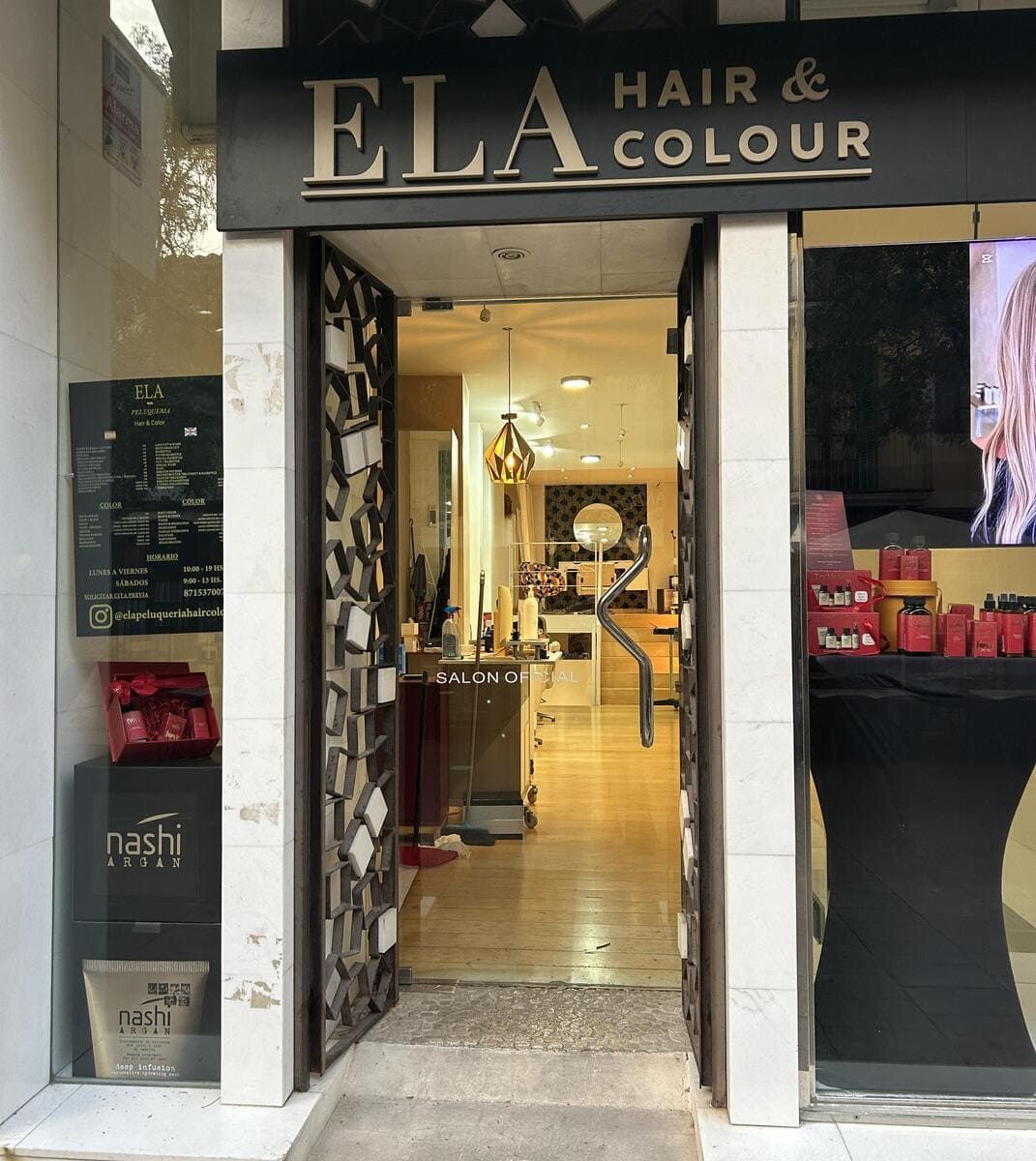 Fachada de peluquería de noche. Exhibición iluminada con cabello rosa. Letrero 