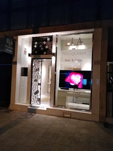 Fachada de peluquería de noche. Exhibición iluminada con cabello rosa. Letrero