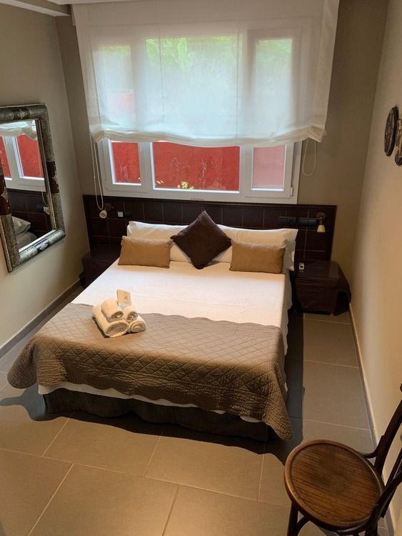 Un dormitorio con cama, silla, espejo y ventana.