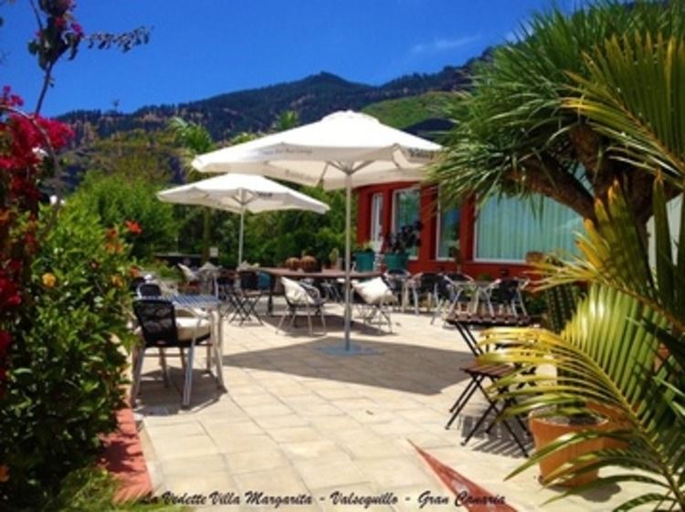Un patio con mesas, sillas y sombrillas con montañas al fondo.