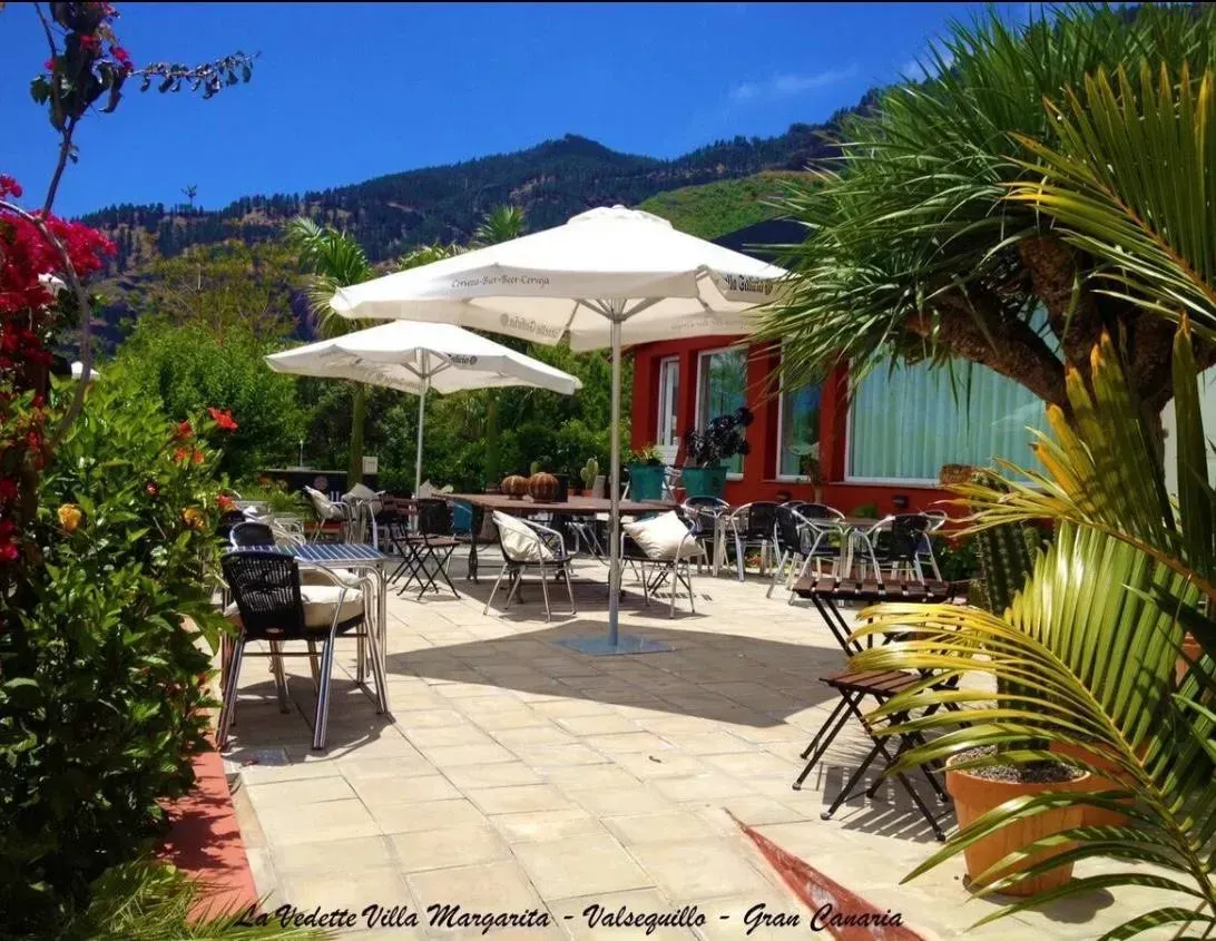 Un patio con mesas, sillas y sombrillas con montañas al fondo.