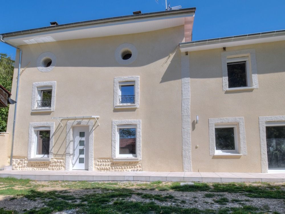 Un bâtiment de deux étages en stuc beige avec une porte d'entrée blanche, des fenêtres rectangulaires et deux fenêtres d'accent rondes.