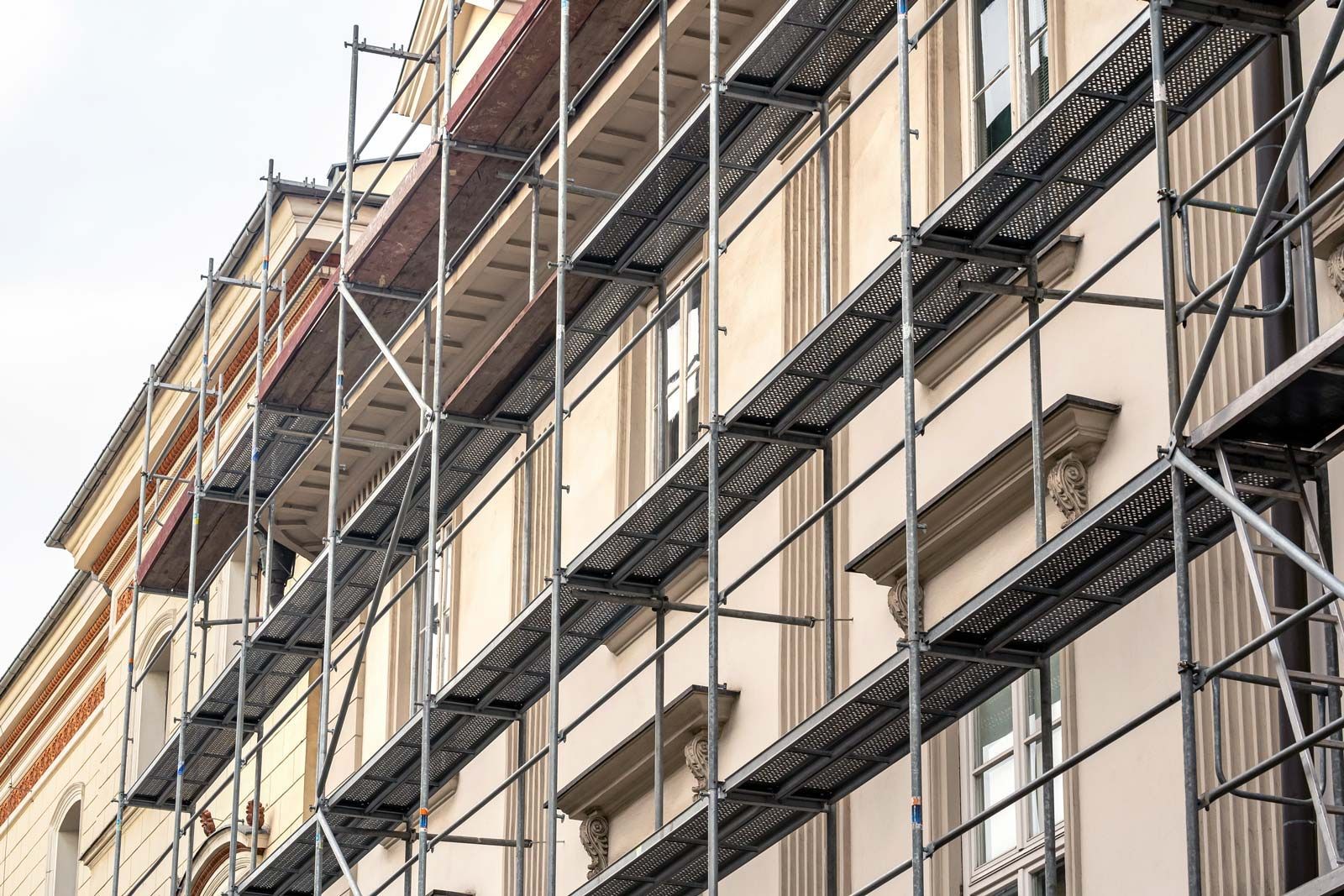 La façade claire d'un immeuble de plusieurs étages est recouverte d'échafaudages métalliques pour des travaux de rénovation extérieure.