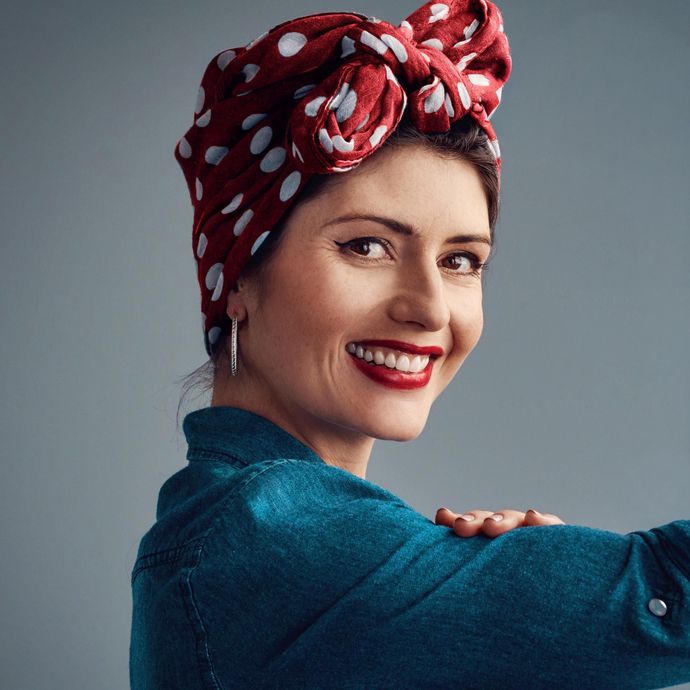 Femme souriante portant un foulard rouge à pois et un chemisier turquoise sur fond gris