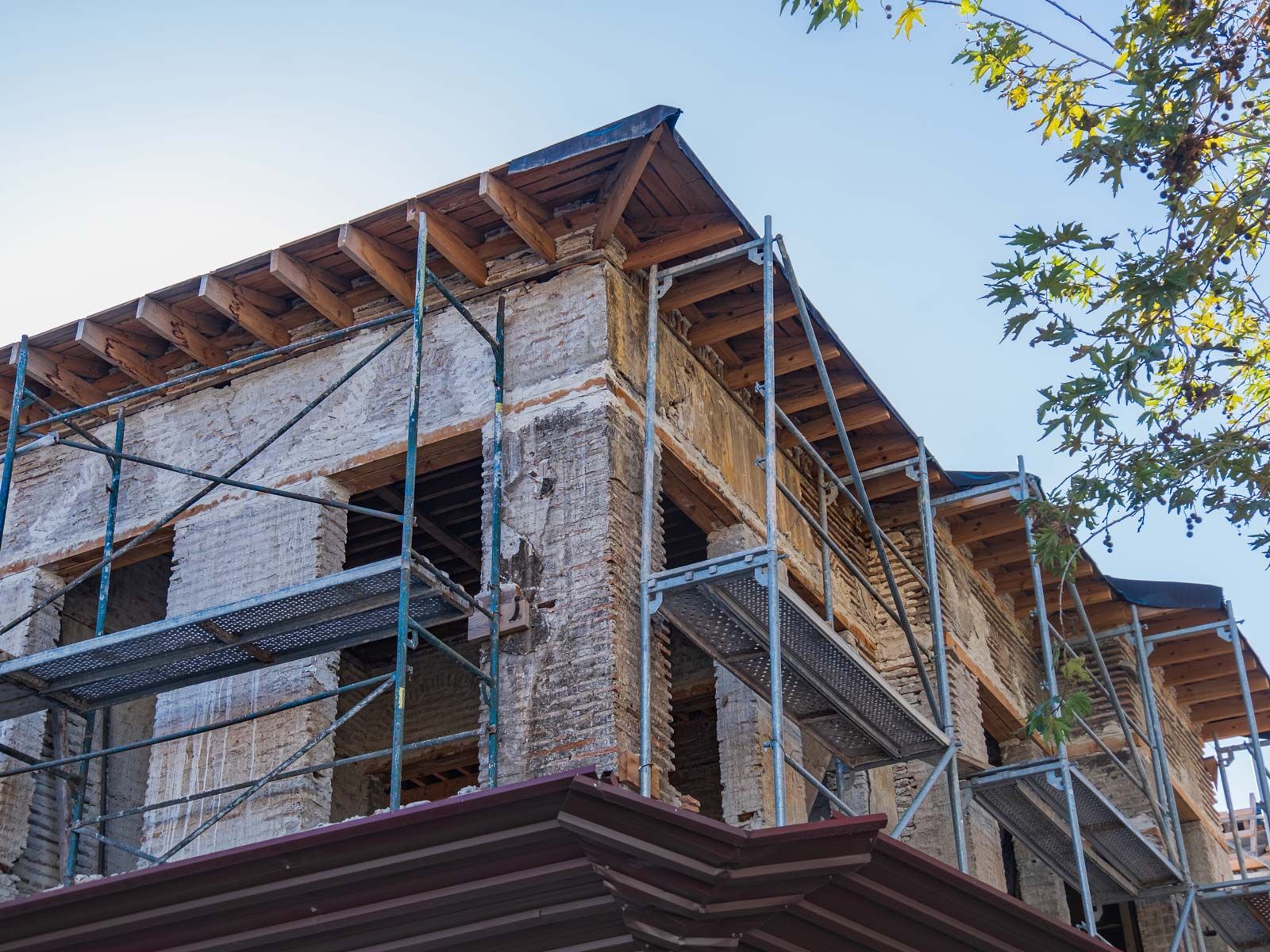 Un bâtiment en briques en cours de rénovation extérieure, enveloppé d'échafaudages métalliques, se détachant sur un ciel bleu azur.