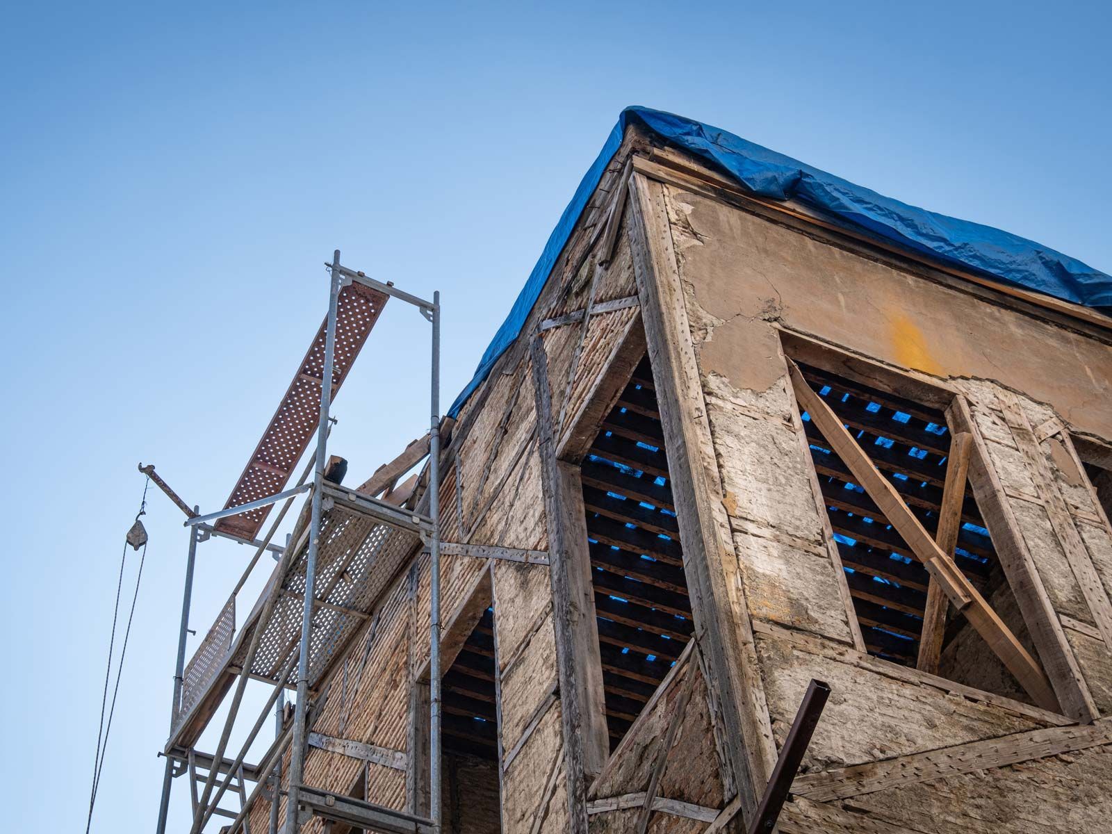 Un vieux bâtiment en pierre en cours de rénovation, avec des échafaudages sur le côté et une bâche bleue recouvrant le toit.