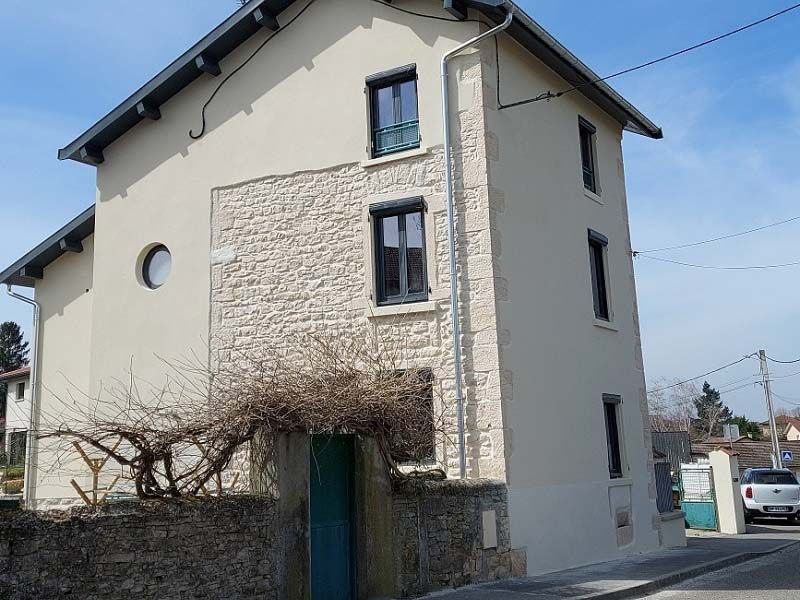 Une maison de trois étages aux murs beiges et présentant sur l'un de ses côtés une section proéminente en pierre texturée de couleur claire.