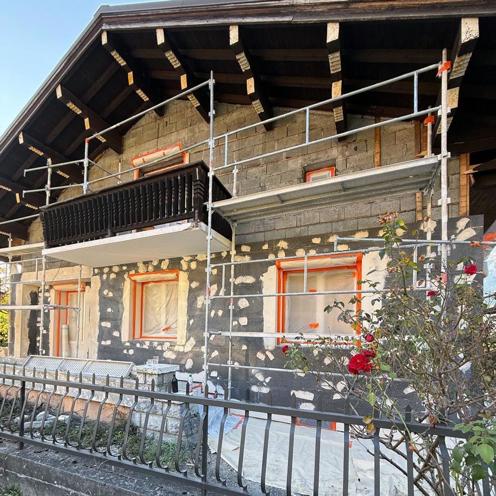 Chalet en pierre avec toit enneigé, fenêtres aux encadrements orange et échafaudages devant un balcon noir