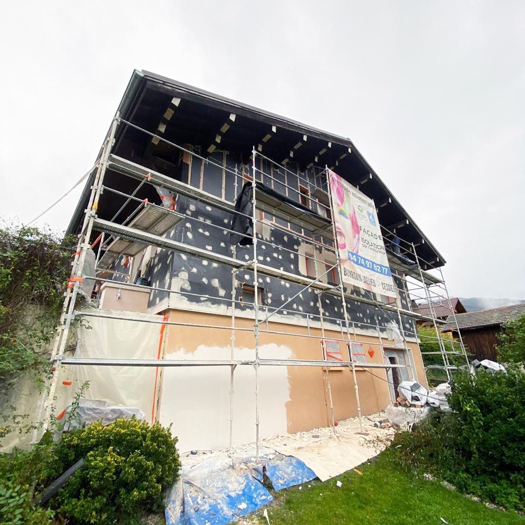 Façade d'une maison en rénovation, entourée d'échafaudages, avec un bardage noir et blanc et des matériaux de construction.