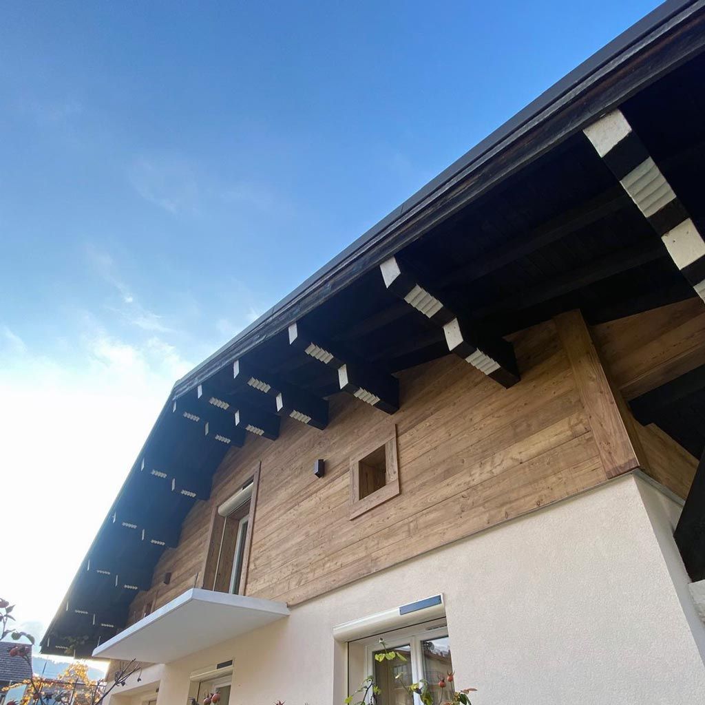 Maison à façade en bois, murs inférieurs blancs et toit sombre et pentu se détachant sur un ciel bleu.