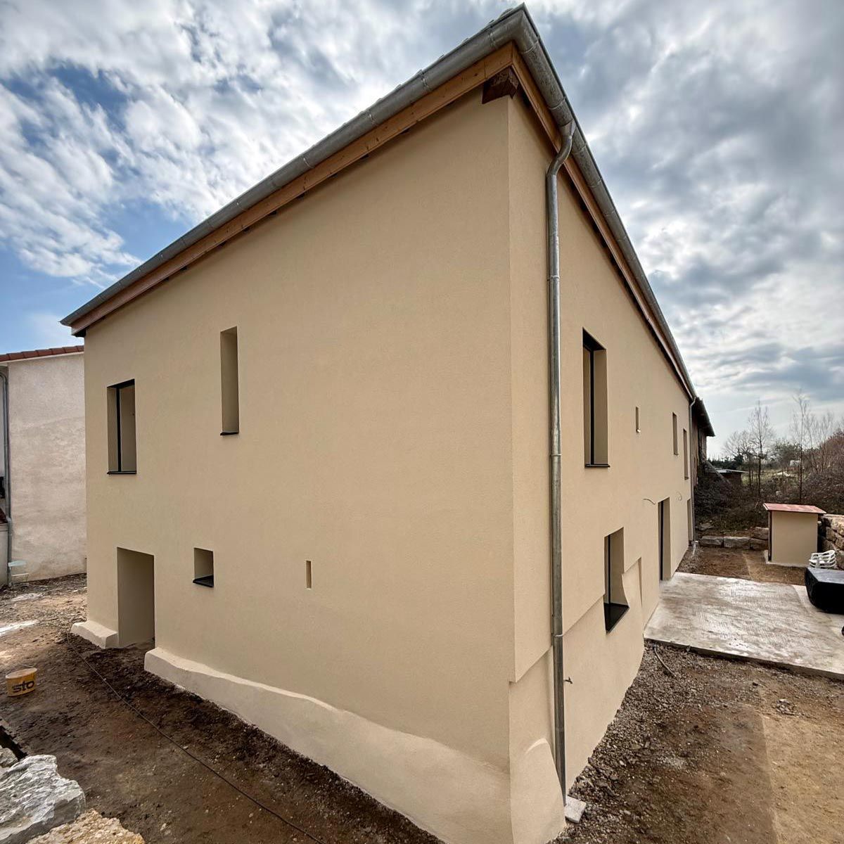 Maison en stuc beige avec petites fenêtres et toit en pente par temps nuageux