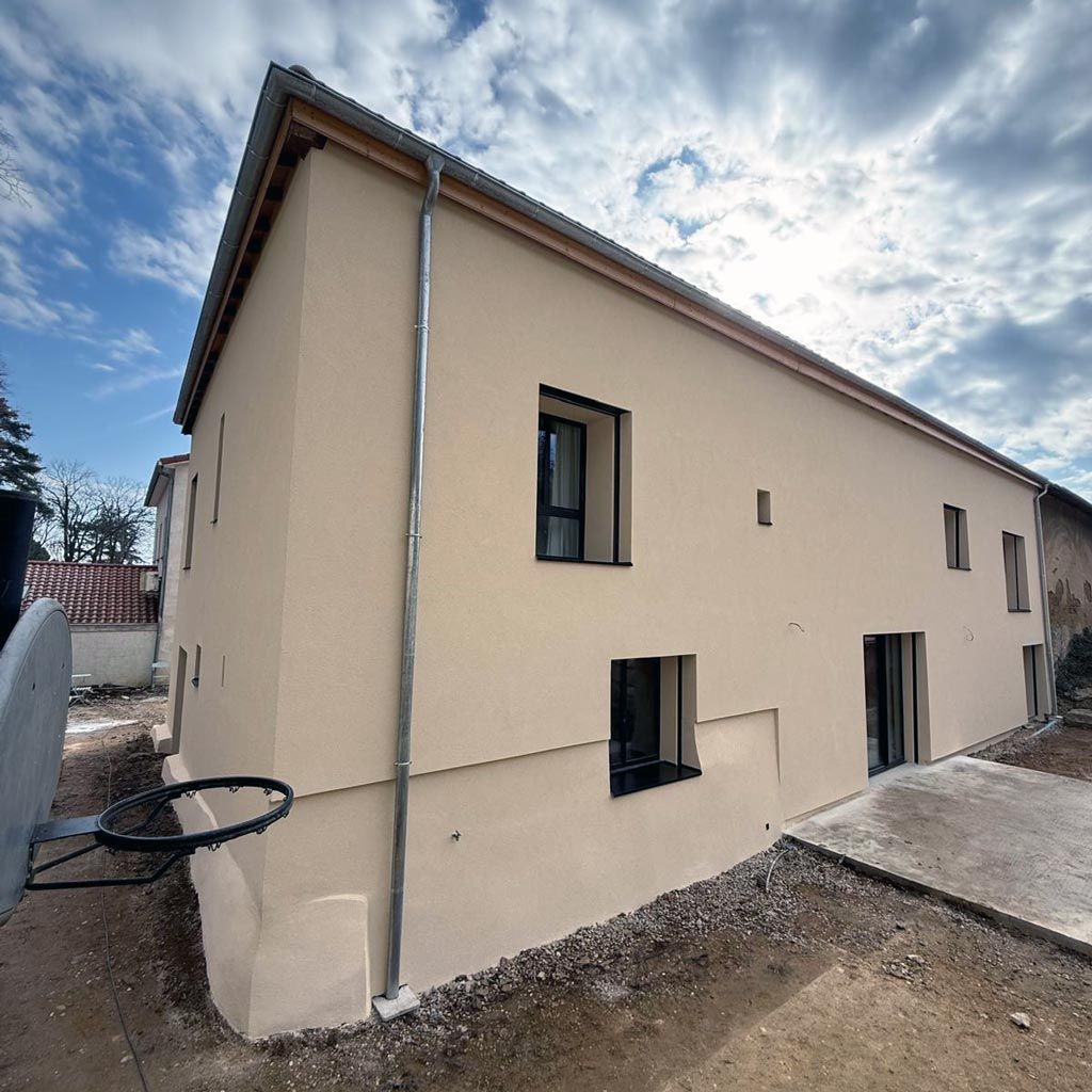 Maison beige à deux étages avec fenêtres à cadre noir sous un ciel nuageux