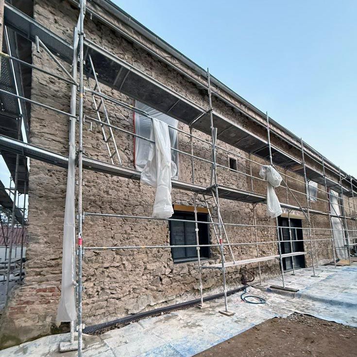 Échafaudages autour d'un bâtiment en pierre en construction, fenêtres occultées et neige au sol.