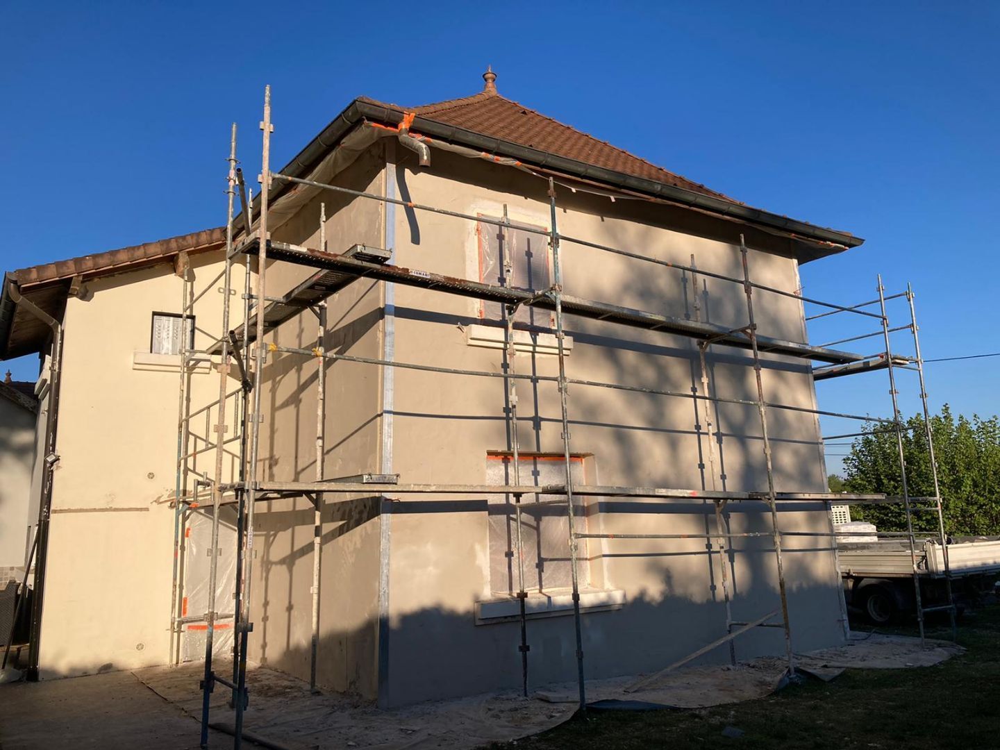 Des échafaudages entourent l'extérieur d'une maison claire en cours de rénovation, sous un ciel bleu azur.