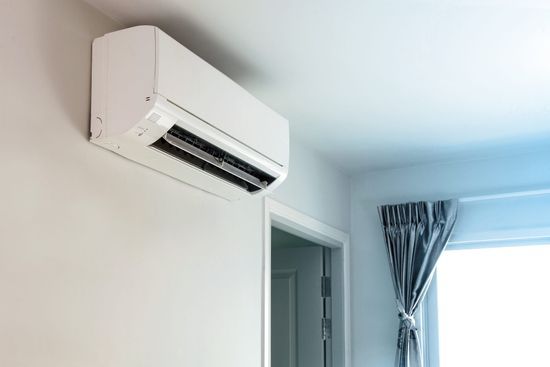 Seinään asennettu valkoinen ilmastointilaite oven yläpuolella valoisassa huoneessa, jossa on ikkuna ja siniset verhot