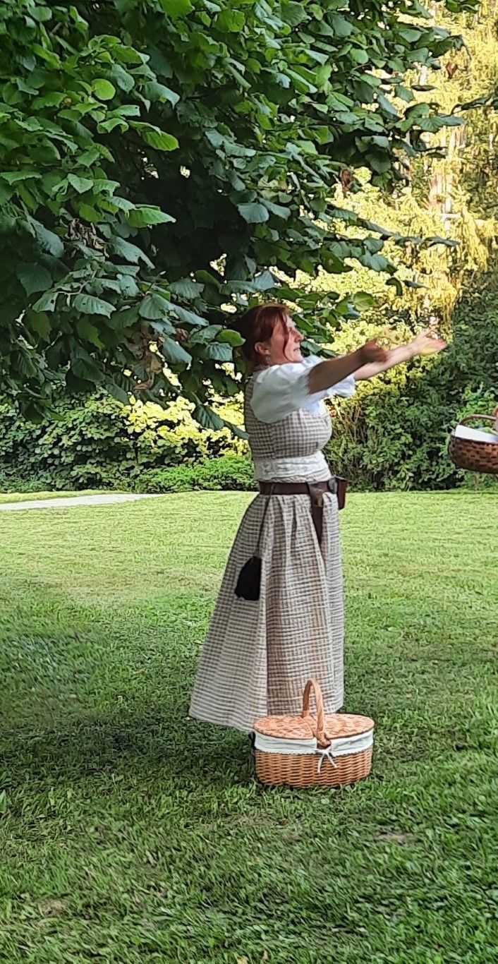 Eine Frau in einem Kleid steht mit ausgestreckten Armen im Gras.