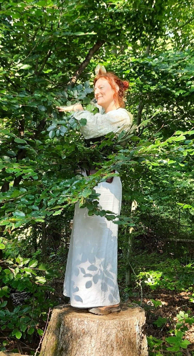 Eine Frau in einem weißen Kleid steht auf einem Baumstumpf im Wald.