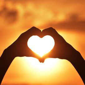 Eine Person formt mit ihren Händen vor der Sonne ein Herz.
