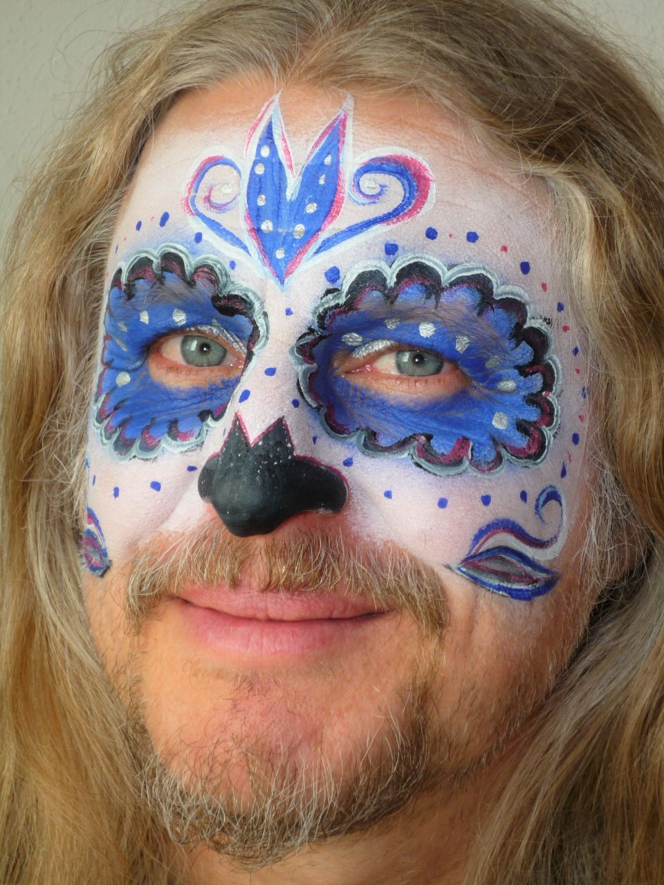 Ein Mann, dessen Gesicht in der Form eines Zuckerschädels bemalt ist.