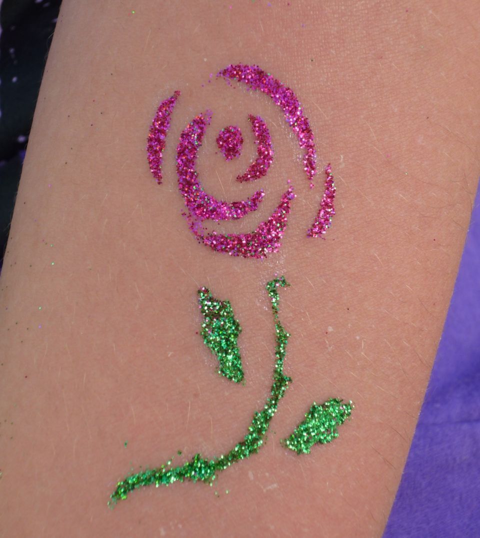 Eine Person hat ein Glitzertattoo einer Rose auf dem Arm.