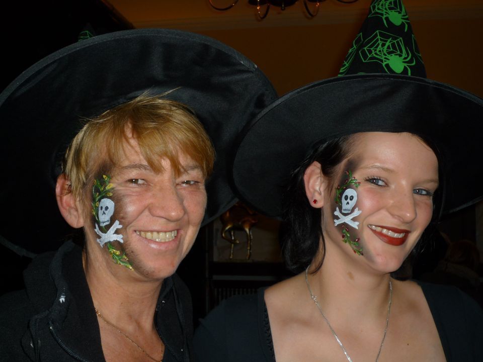 Zwei Frauen tragen Hexenhüte mit Totenköpfen und gekreuzten Knochen auf ihren Gesichtern gemalt