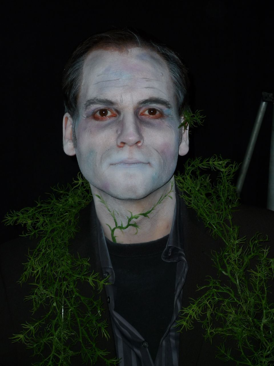 Ein Mann mit blauer Farbe im Gesicht steht neben einer Pflanze.