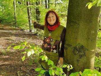 Eine Frau steht neben einem Baum im Wald.