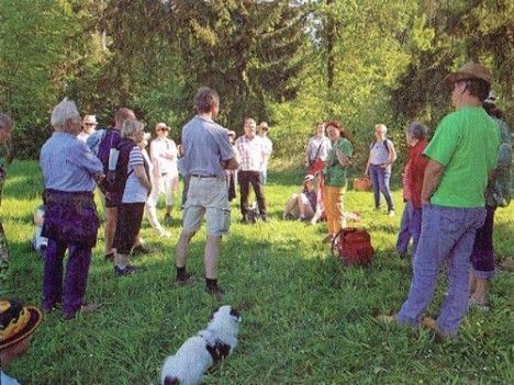 Eine Gruppe von Menschen steht auf einer Wiese mit Bäumen im Hintergrund.