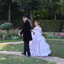 Ein Mann mit einem schwarzen Hut geht mit einer Frau in einem weißen Kleid spazieren.