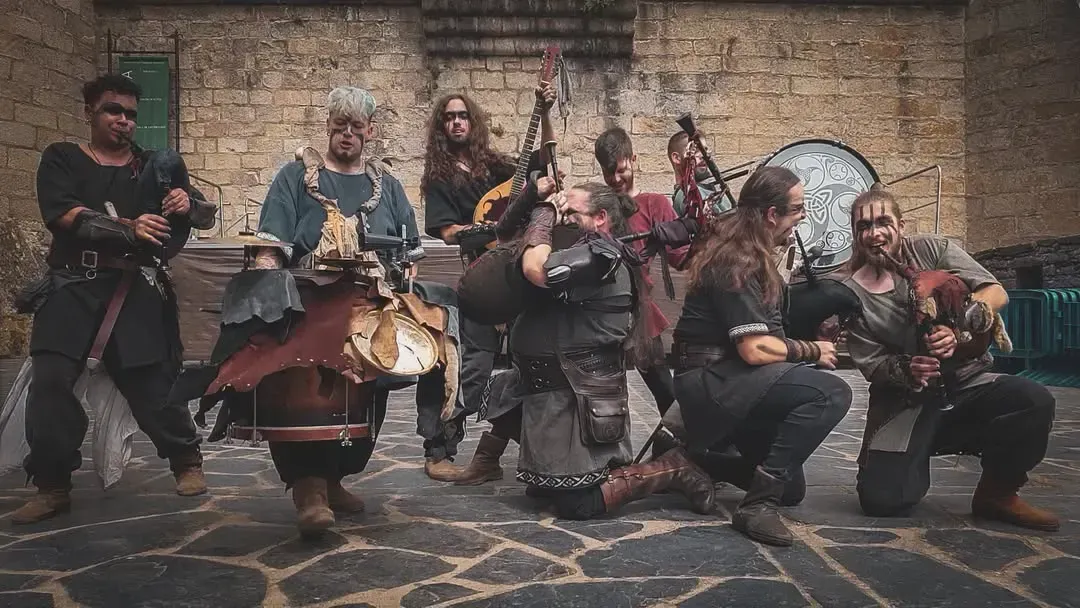 Un grupo de personas disfrazadas con instrumentos posan al aire libre contra un muro de piedra