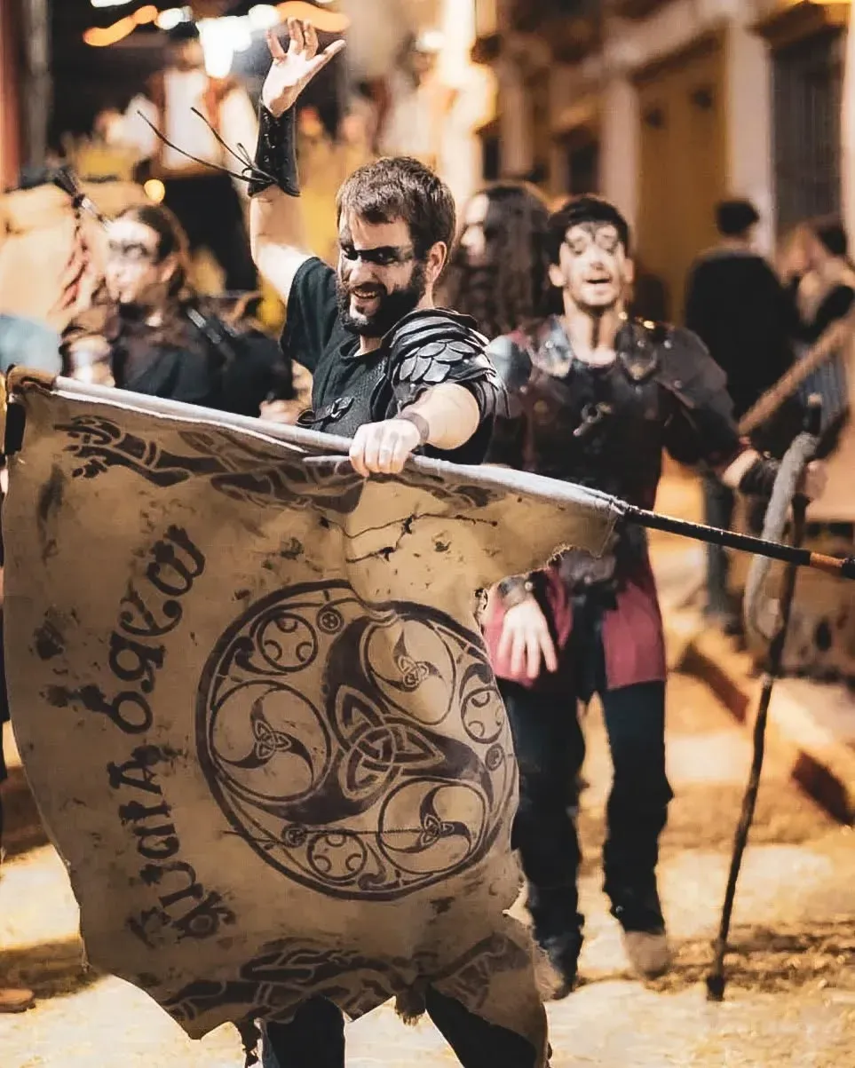 Un hombre toca la gaita, vistiendo un sombrero ribeteado de piel, un chaleco rústico 