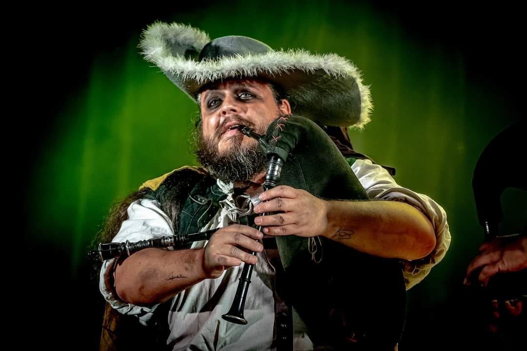 Un hombre toca la gaita, vistiendo un sombrero ribeteado de piel,