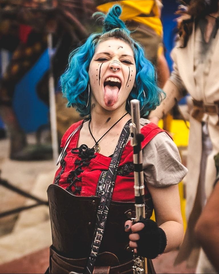 Dos hombres con atuendos medievales tocan instrumentos de cuerda al aire libre. Uno con una mandolina y el otro con un bajo.