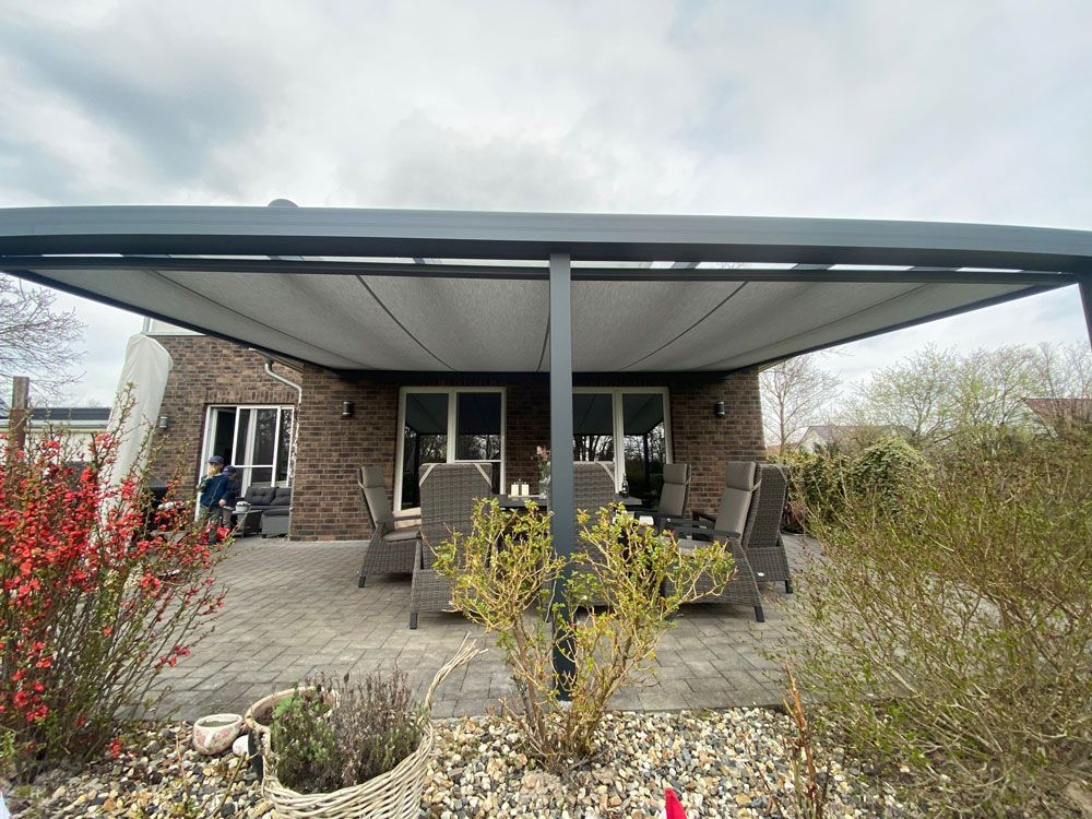Terrasse mit ausfahrbarer Markise, Sitzgelegenheiten im Freien und ein Backsteinhaus unter bewölktem Himmel.