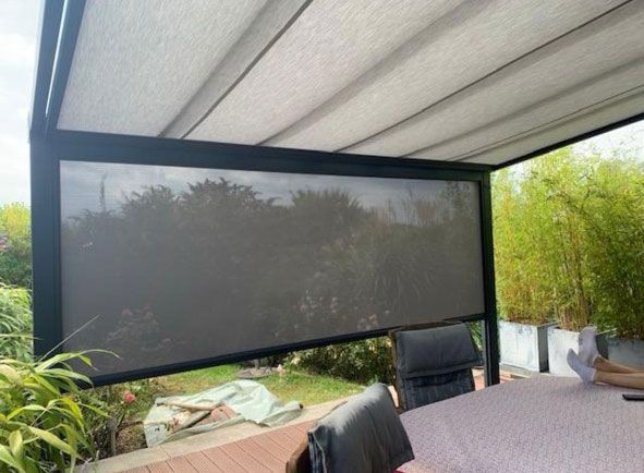 Pergola mit einziehbarem Dach und herabgelassener dunkler Leinwand über einer Terrasse, Sitzgruppe im Freien.