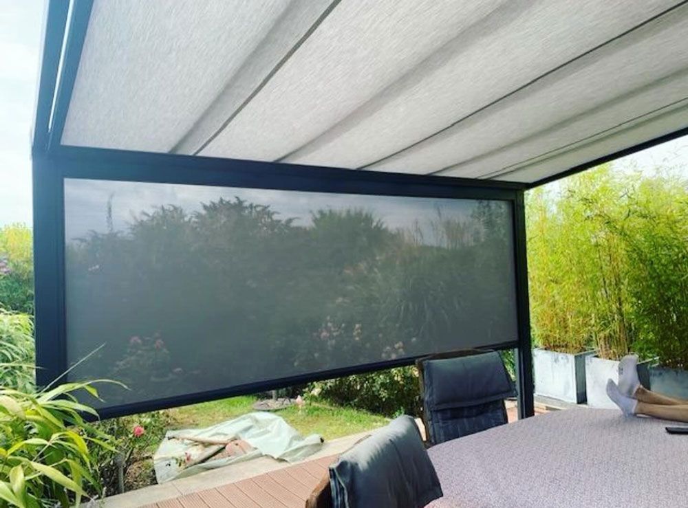 Pergola mit einziehbarem Sichtschutz, Sitzgelegenheiten im Freien und Blick auf einen Garten.