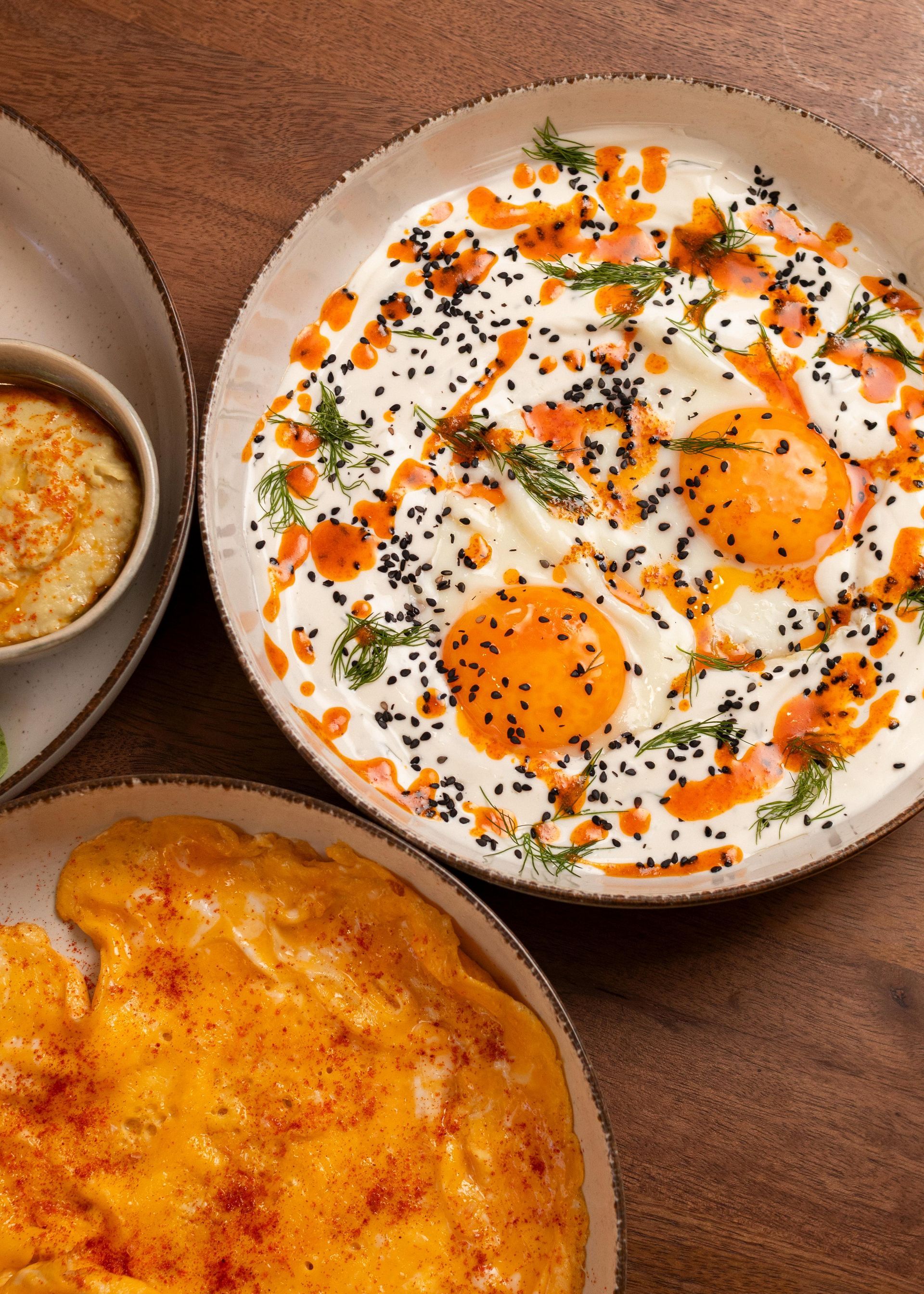 Platos de desayuno con huevos fritos, tostadas y un plato pequeño sobre una mesa de madera.