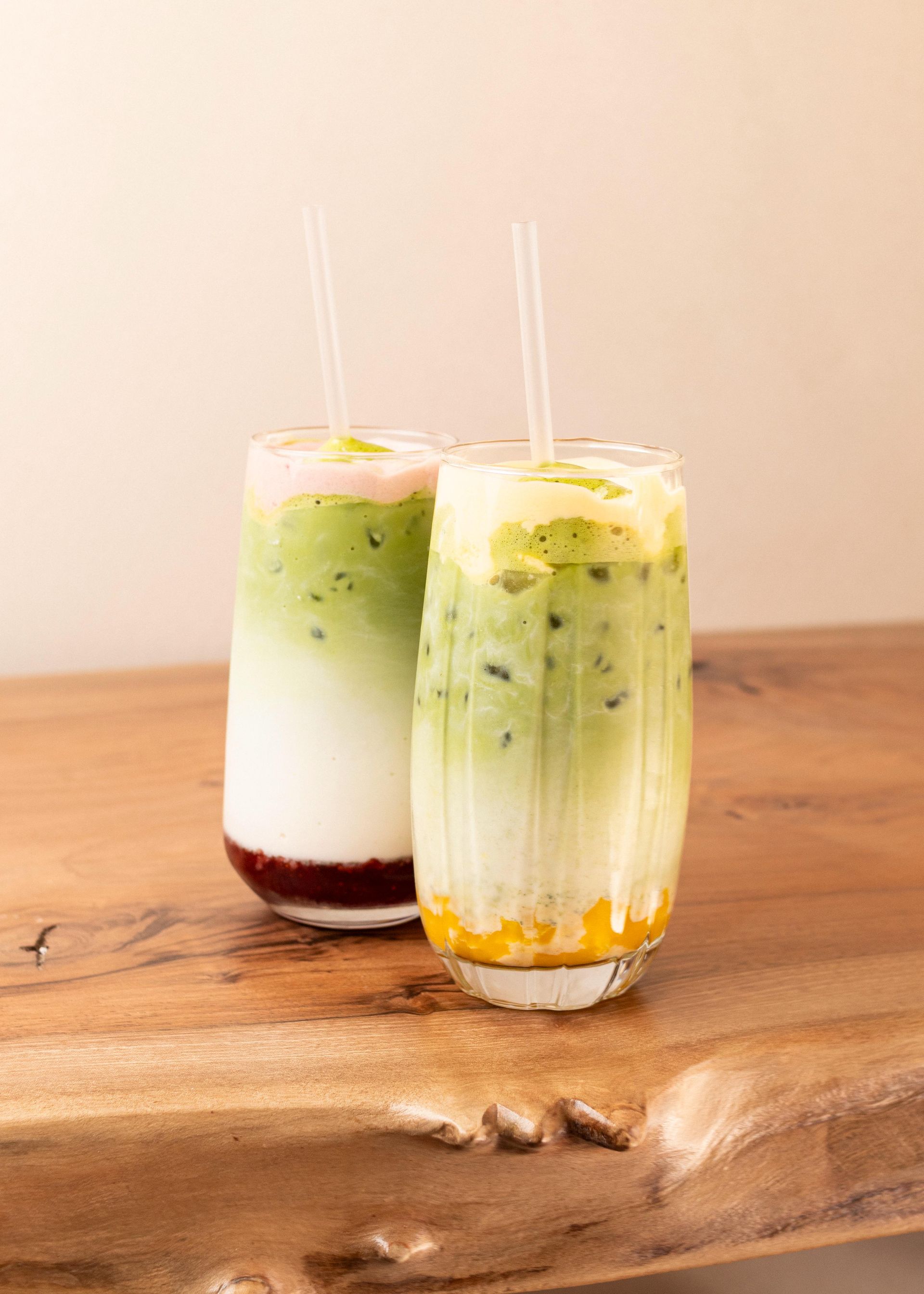 Dos bebidas heladas de capas verdes y blancas en vasos transparentes con pajitas sobre una mesa de madera.