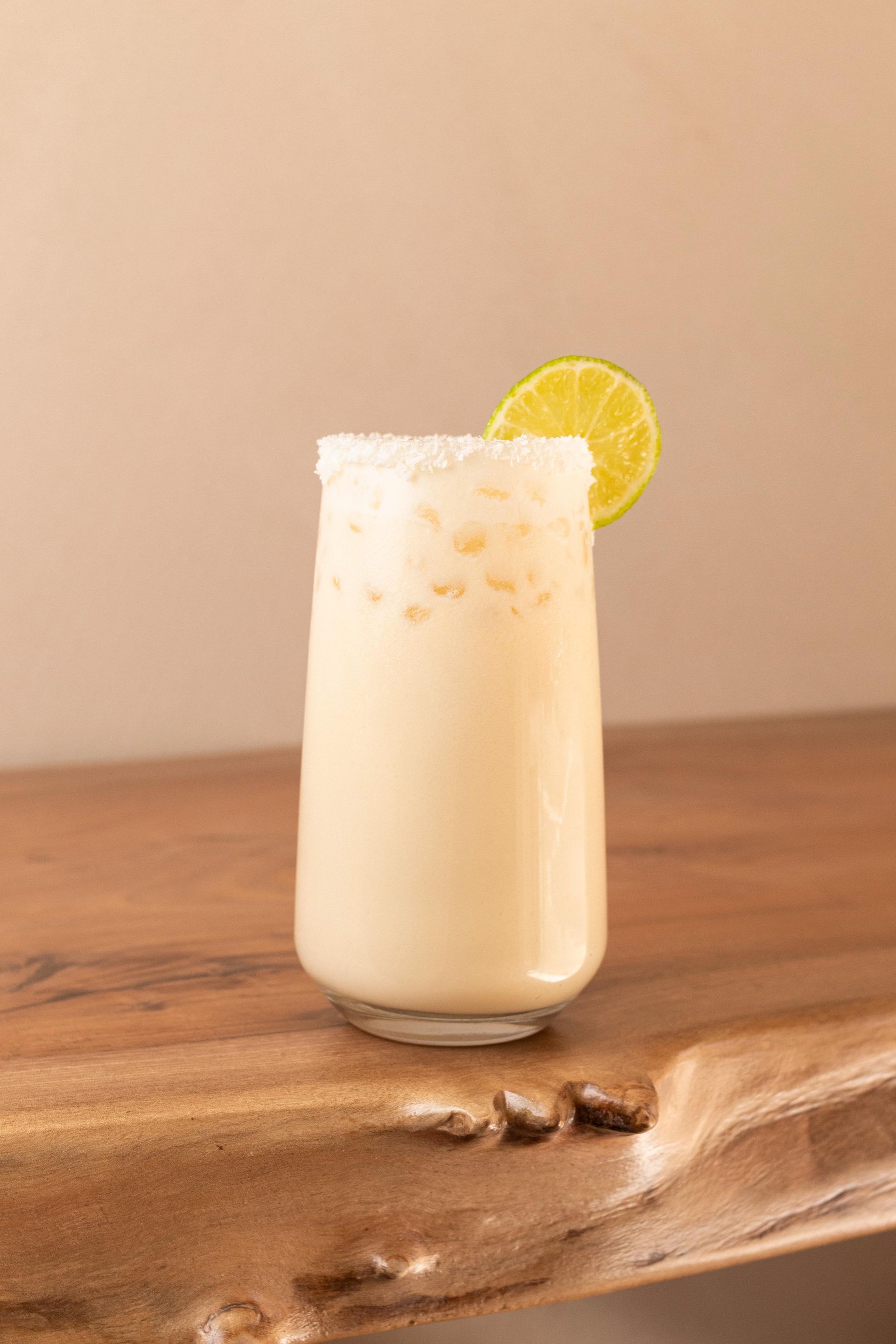 Bebida cremosa helada en un vaso alto con una rodaja de limón sobre una mesa de madera.