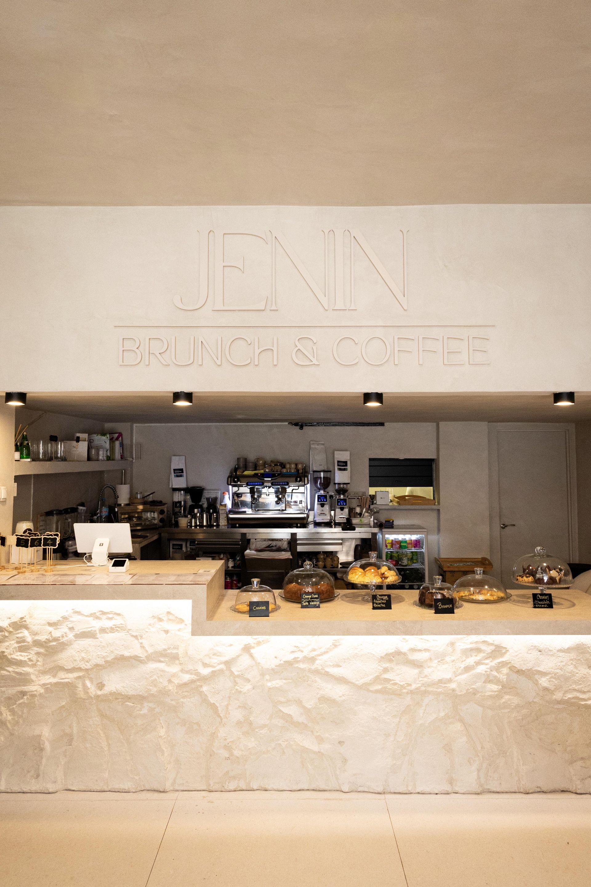 Mostrador minimalista de JINN para brunch y café, con frontal de piedra beige y equipo de espresso cuidadosamente dispuesto.