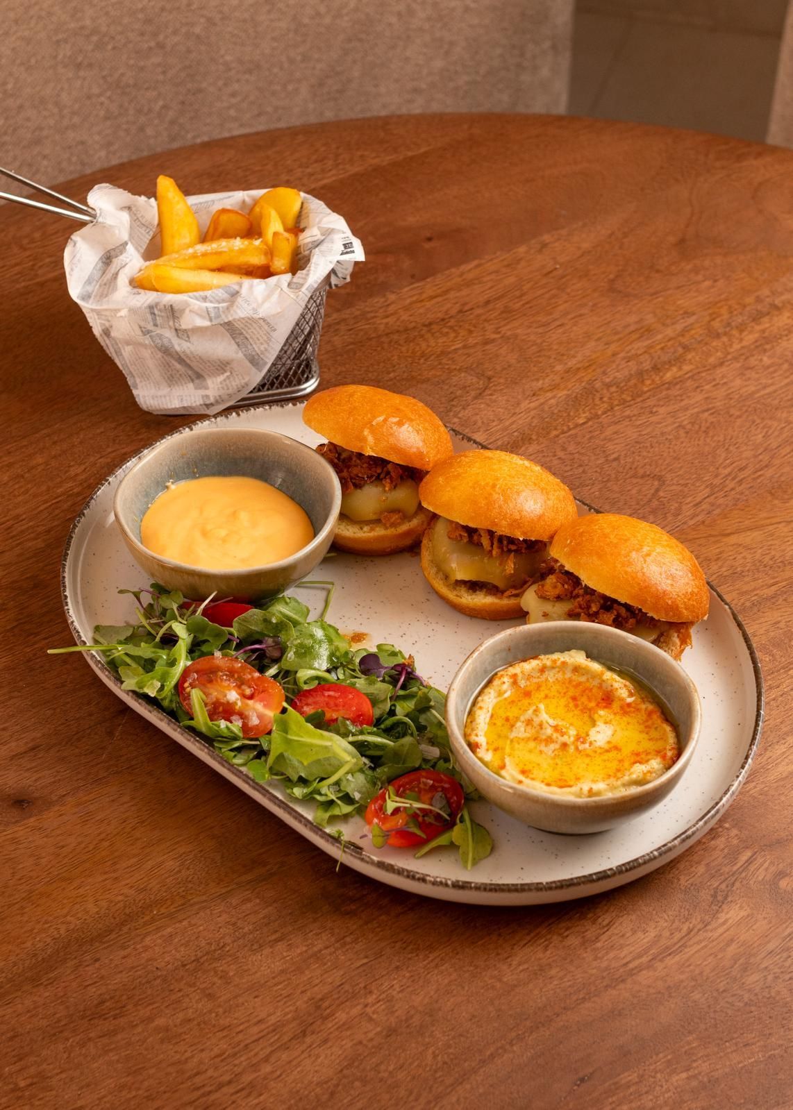 Brioches y patatas fritas en una mesa de madera con ensalada, salsas para mojar y una taza de salsa de queso.
