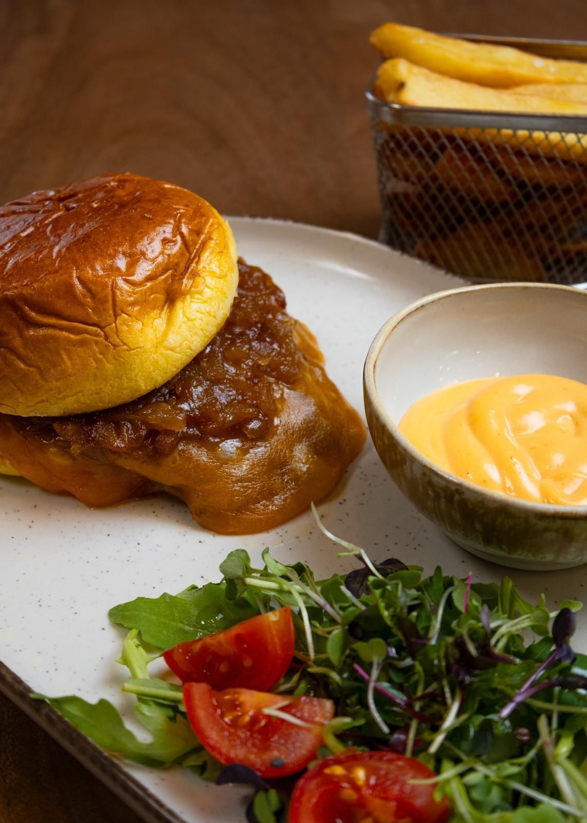 Brioches y patatas fritas en una mesa de madera con ensalada, salsas para mojar y una taza de salsa de queso.