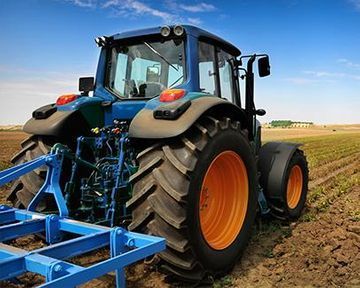 Tractor azul arando un campo bajo un cielo azul claro.