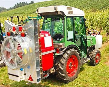 Tractor verde con pulverizador rojo y blanco en un viñedo.